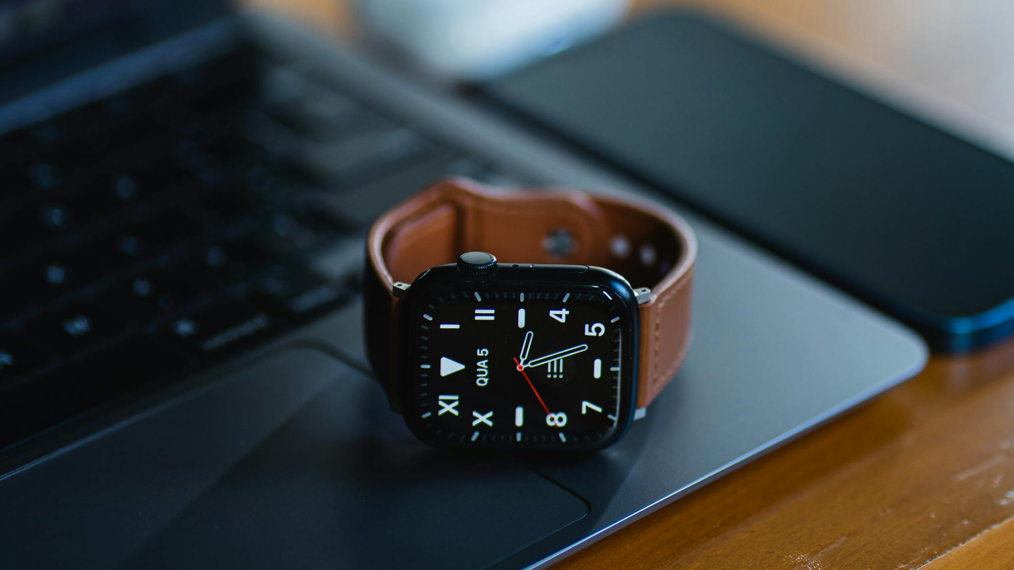 A modern smartwatch with a brown leather band sits on a laptop, showcasing sleek technology design.