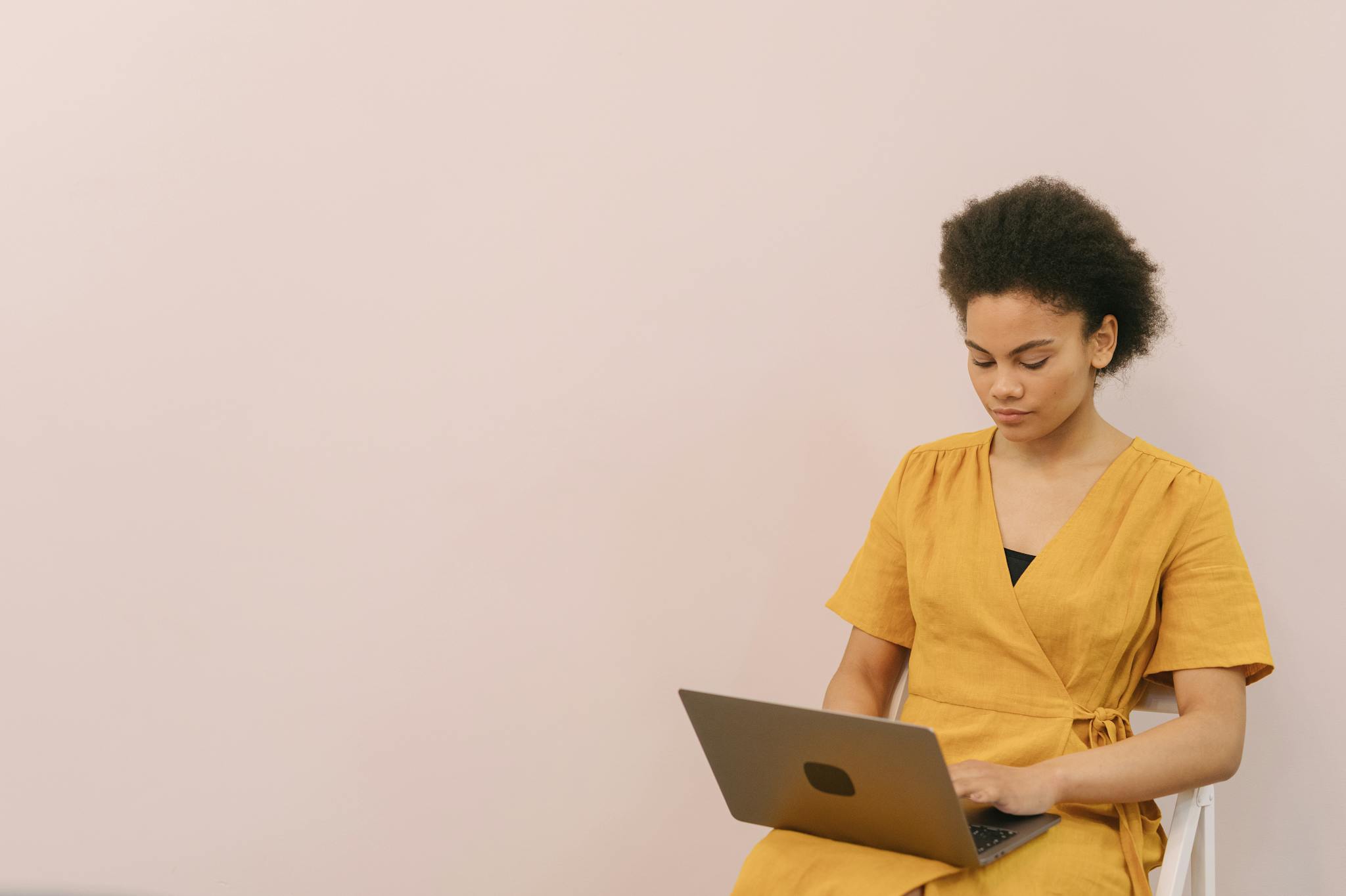African American woman working on a laptop indoors, in a minimalist setting.